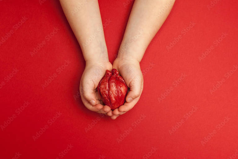 Coração humano em mãos de crianças isoladas em fundo vermelho