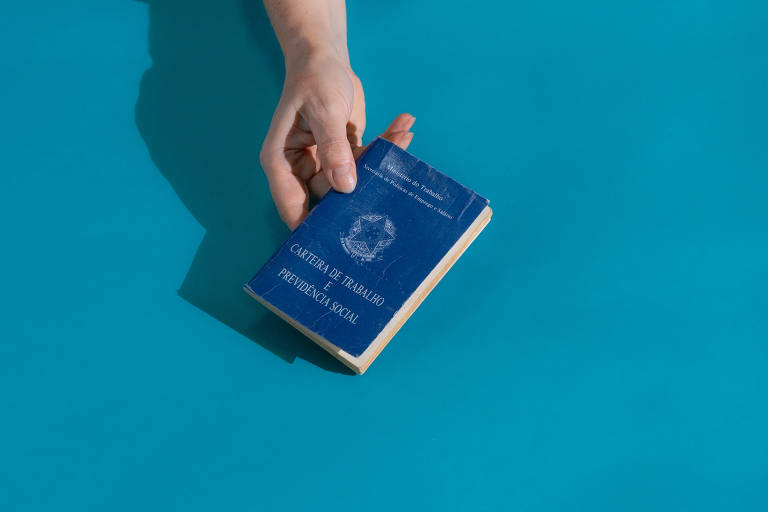 Uma mão segura uma carteira de trabalho brasileira sobre um fundo azul