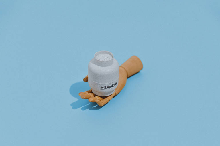 Mão de madeira segura botijão de gás em miniatura sob fundo azul 