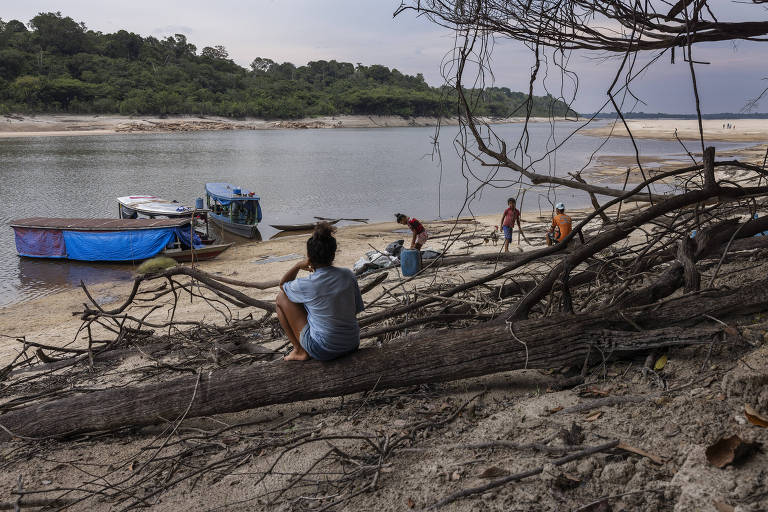 Pessoas sentadas na margem de um rio com canoas na beira da água