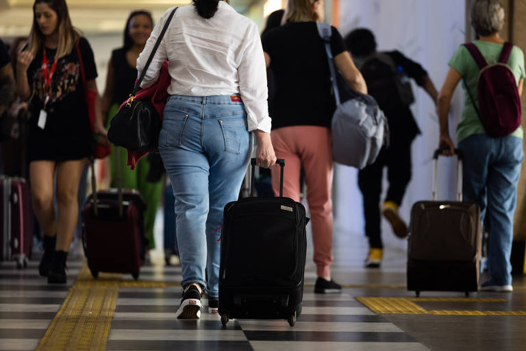 Passageiros de costas carregam malas em aeroporto de Congnhas