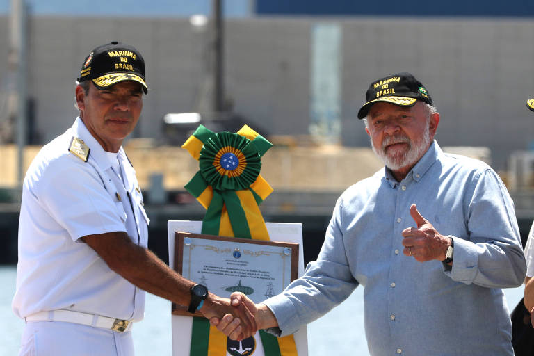 Homem idoso branco de barba, com boné, aperta as mãos de oficial da Marinha