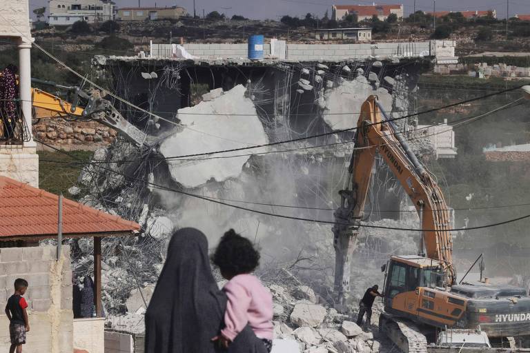 Mulher palestina segura criança enquanto assiste a demolição de prédio por forças de Israel na cidade de Hebron, na Cisjordânia ocupada