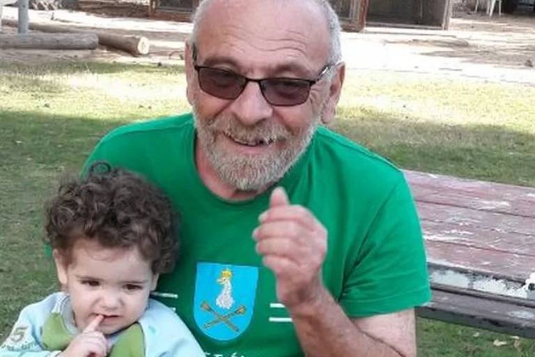 alex, idoso, calvo, usa óculos escuros e camiseta verde, sorri para foto com a neta