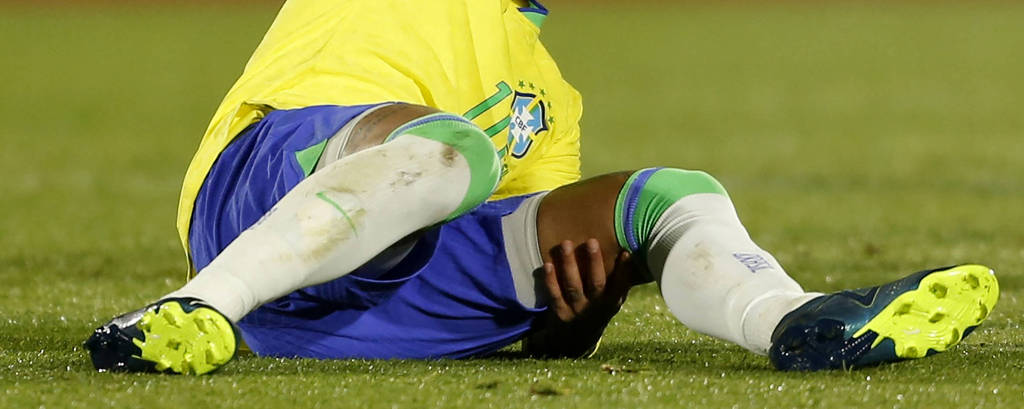 Neymar leva a mão esquerda até a perna ao machucar o joelho em Uruguai x Brasil, no estádio Centenario de Montevidéu