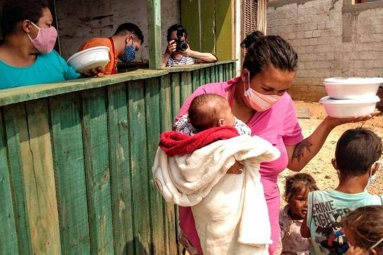 Mulher com filhos recebendo marmita durante a pandemia de covid-19
