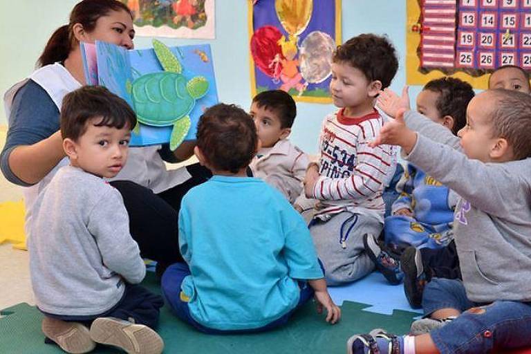 Educadora e crianças lendo um livro infantil em creche municipal
