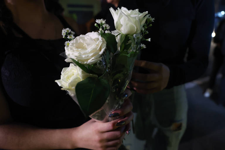 Imagem mostra flores brancas nas mãos de uma jovem que veste roupa preta