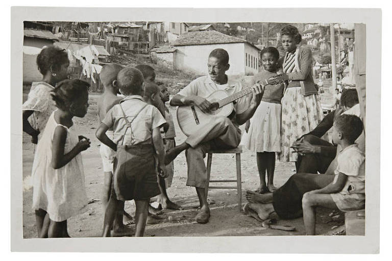 Em foto preto e branco, o sambista Cartola aparece tocando violão ladeado de crianças