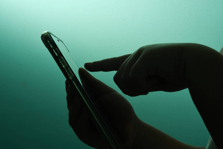 Silhueta de mãos de criança mexendo em um smartphone, em um cenário esverdeado.
