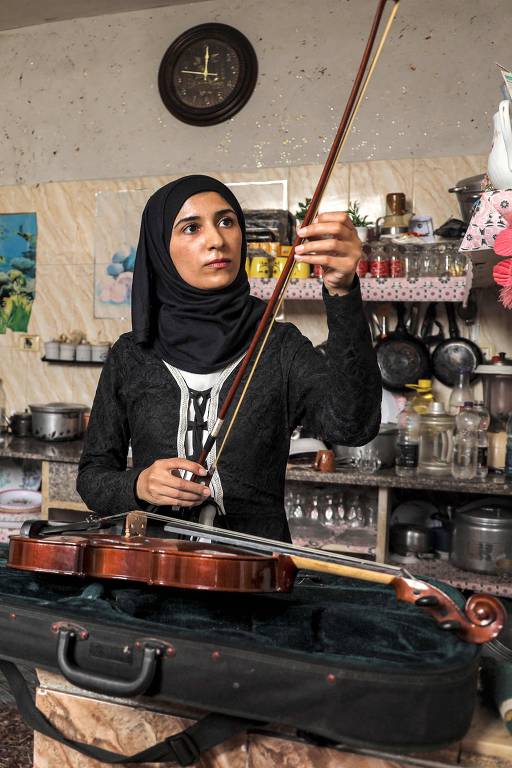 A musicista palestina Jawaher al-Aqraa mexendo em seu violino na cozinha de casa em Deir al-Balah, no centro de Gaza