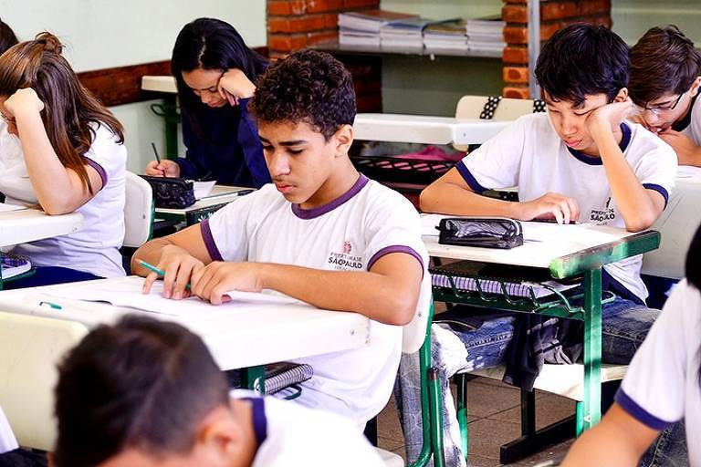 Estudantes sentados em carteiras preenchem questões de prova