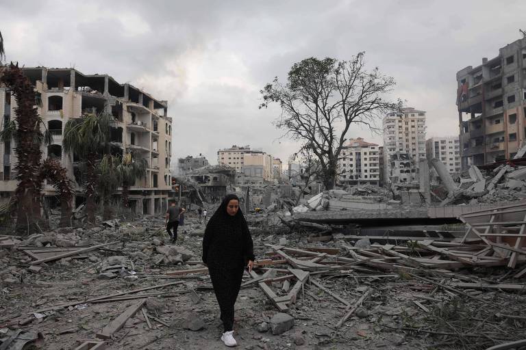 Palestinos andam sobre os escombros do bairro Rimal, na Cidade de Gaza, após os ataques de Israel em 10 de outubro