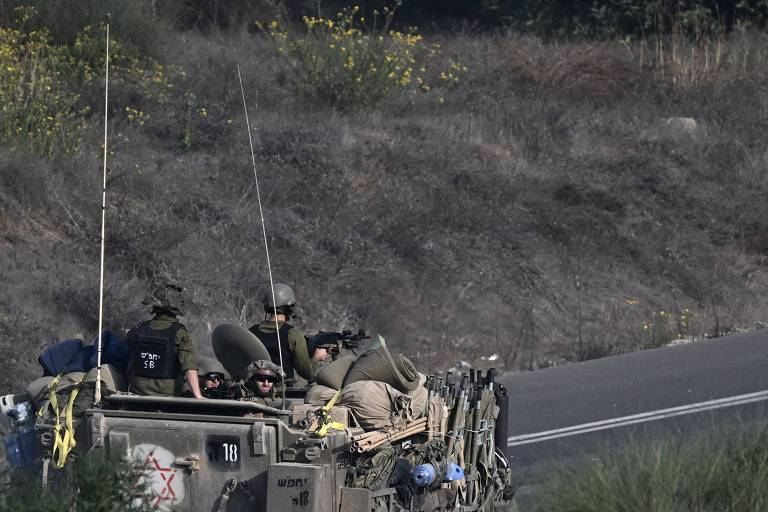 Veículo de guerra com soldados anda por uma estrada que corta uma região arborizada