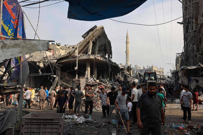 Moradores ao redor de área destruída por ataques aéreos no campo de refugiados de Al-Shatee, na Cidade de Gaza