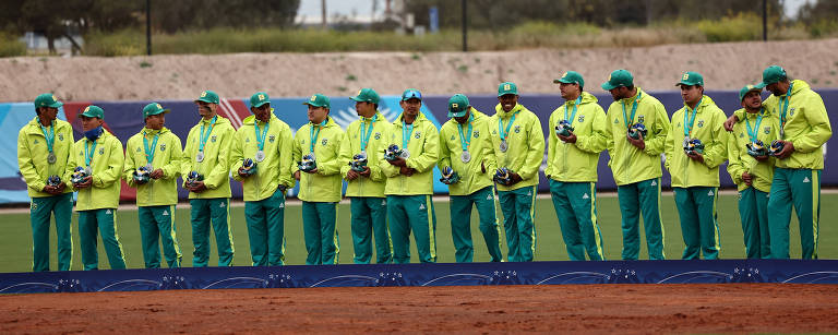 O time, uniformizado com jaquetas, calças e bonés verdes, lado a lado no pódio. 