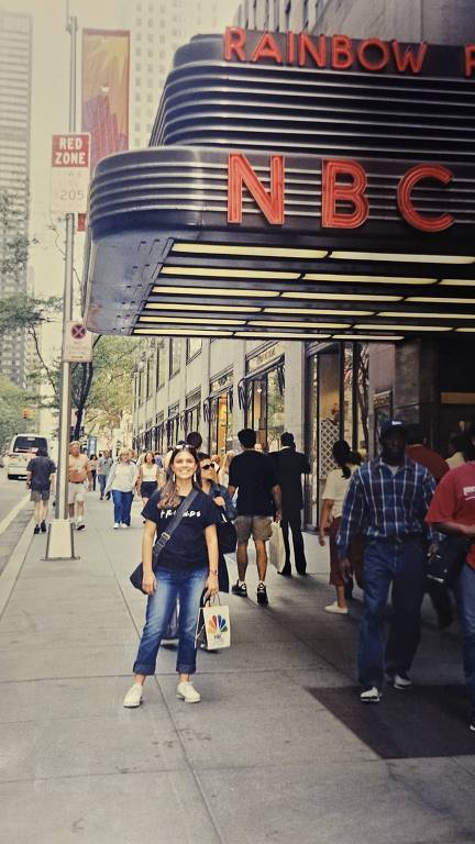 Mulher branca usa camiseta preta com escrito Friends em frente à rede de TV NBC em Nova York