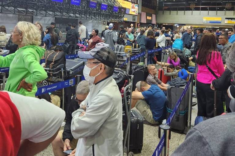 A imagem mostra pessoas em pé em um aeroporto