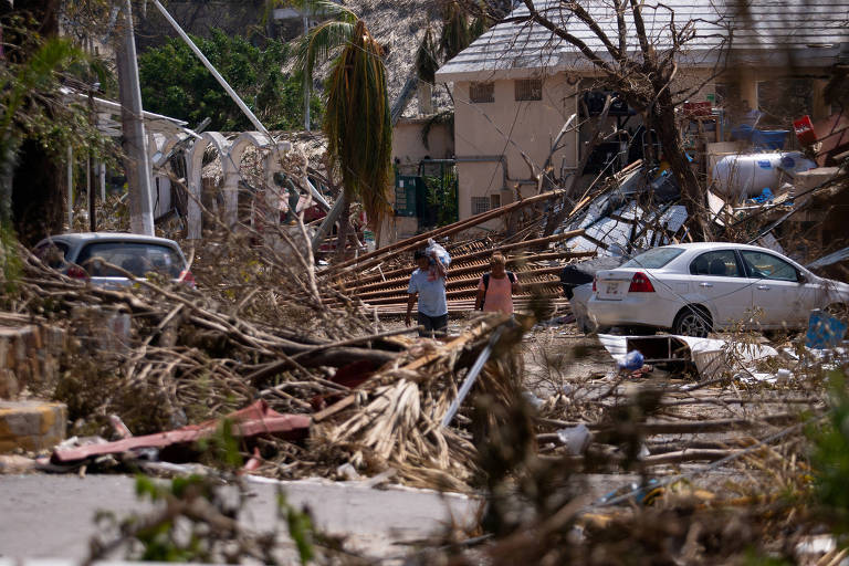 Pessoas caminham ao lado de escombros e árvores danificadas após a passagem do furacão Otis, em Acapulco, no México