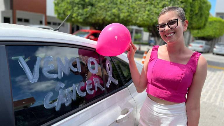 Bianca Lopes ao lado de um carro; no vidro, lê-se: "Venci o câncer."