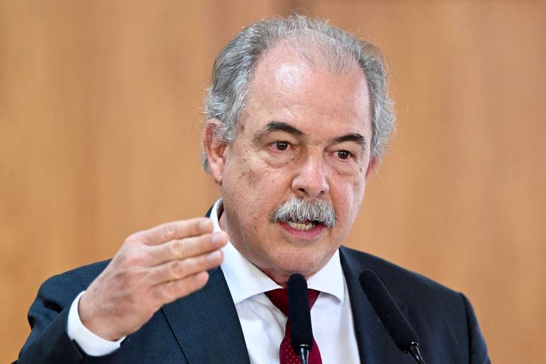 Aloizio Mercadante, presidente do BNDES; ele é um homem branco, com cabelos grisalhos, de bigode, usa um terno azul marinho, camisa branca e gravata vermelha e aponta com a mão direita