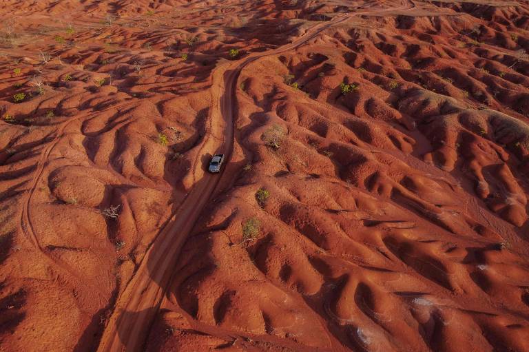 Vista de drone de carro andando em estrada de terra em um deserto de terra vermelha e ondulada