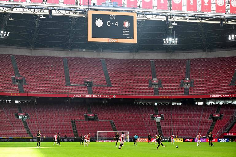 Jogadores de Ajax e Feyenoord atuam em estádio sem público para completar partida interrompida três dias antes porque torcedores lançaram sinalizadores no campo; o placar mostra 4 a 0 para o Feyenoord