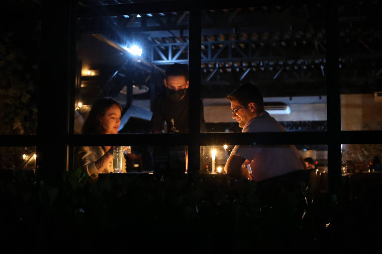 Imagem mostra duas pessoas iluminadas por velas no interior de um prédio 