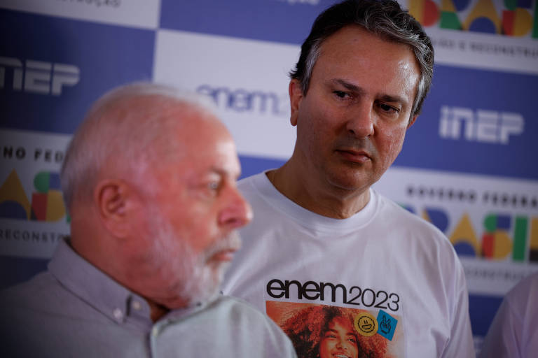 foto colorida mostra Lula, um senhor de cabelos e barba branca, de camisa e perfil, à frente de Camilo Santana, que é mais alto, cabelos pretos, e com uma camiseta onde se lê Enem 2023