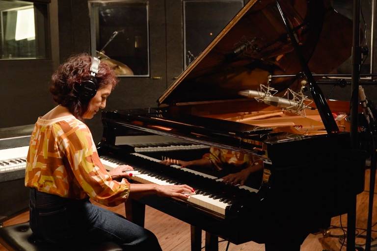 Em foto colorida, a pianista, arranjadora e compositora Marta Karassawa aparece tocando piano