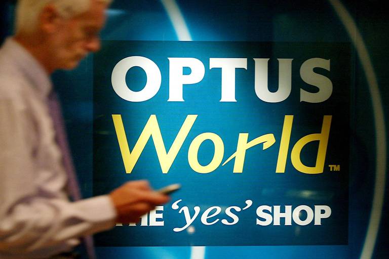 Homem tenta usar celular em frente a painel da Optus, operadora de celular na Austrália