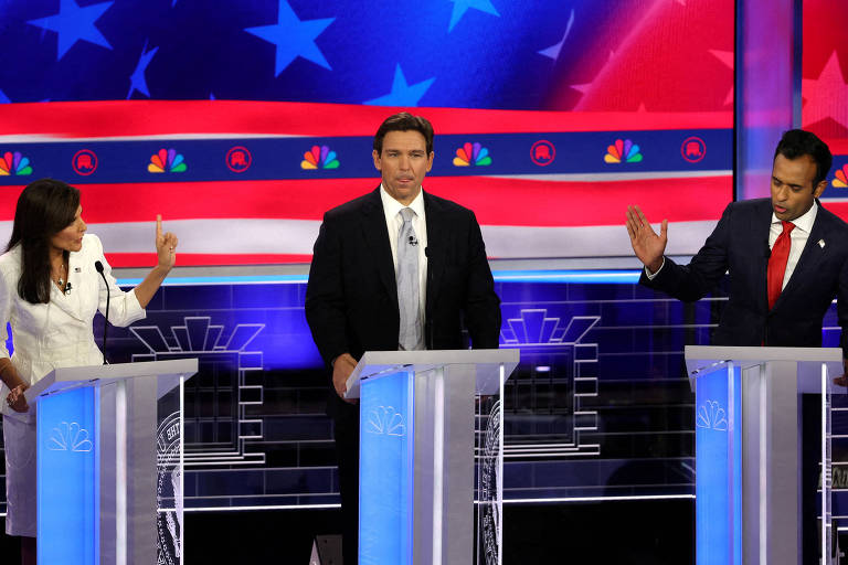 Três políticos, cada um em um púlpito individual, frente a projeção nas cores da bandeira dos EUA