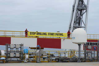 Greenpeace activists stand with a banner on a Shell oil production vessel in the Atlantic Ocean