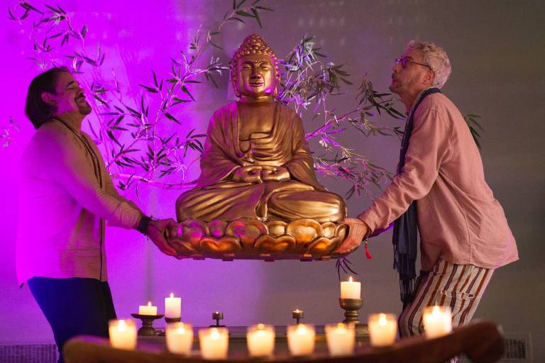 Em foto colorida, dois homens aparecem carregando uma imagem de Buda
