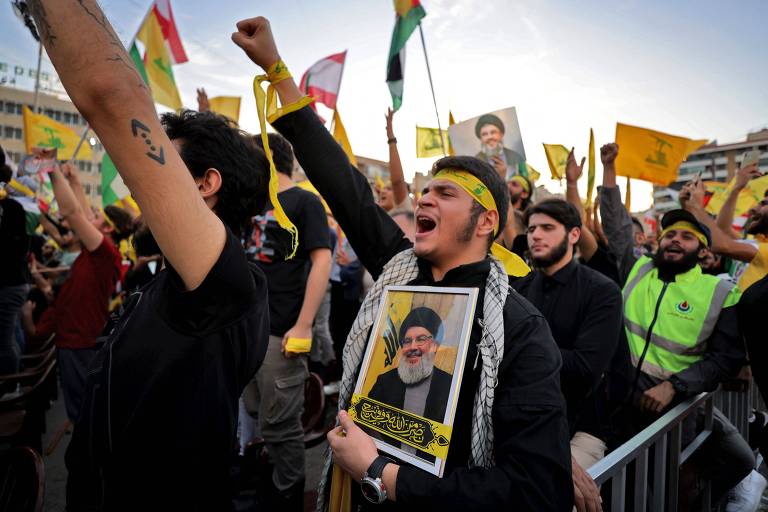 Apoiadores nos subúrbios do sul de Beirute, no Líbano, com bandeiras do Hezbollah e retratos de Hassan Nasrallah, líder do grupo, durante primeiro pronunciamento dele, que foi televisionado
