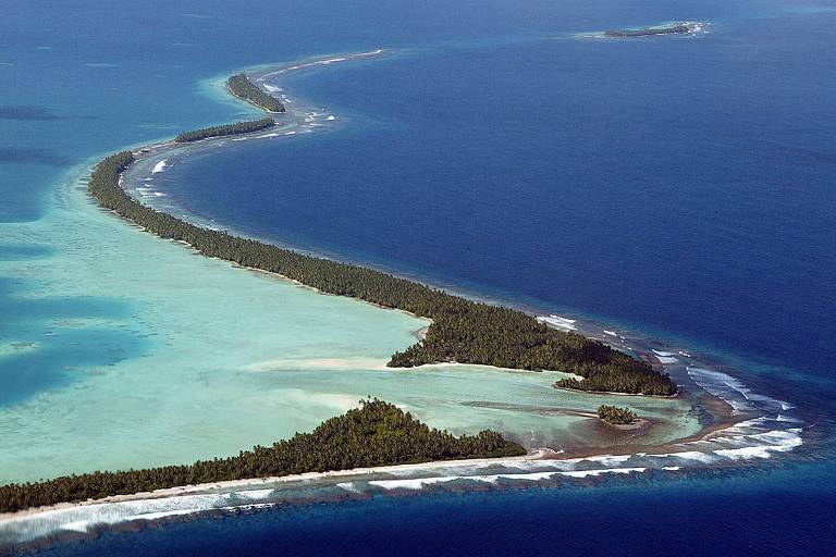 Vista aérea de atol em formato de S cercado pelas águas azuis do oceano Pacífico