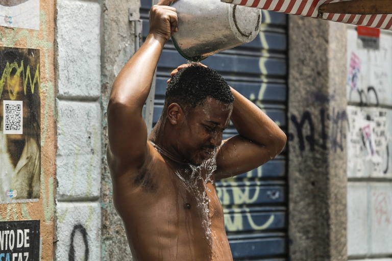 jovem negro, sem camisa, joga água na própria cabeça usando balde de metal