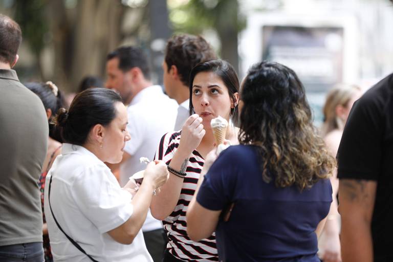 Três mulheres tomam sorvete em meio a outras pessoas