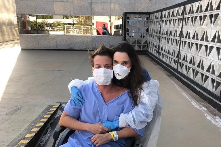Rafael, homem branco, veste roupa hospital azul e está em uma cadeira de rodas, abraçado por sua irmã, Ana, mulher branca. Ambos usam máscaras em razão da pandemia