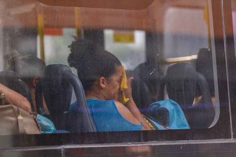 Dentro de ônibus, mulher usando blusa azul seca o suor do rosto com lenço
