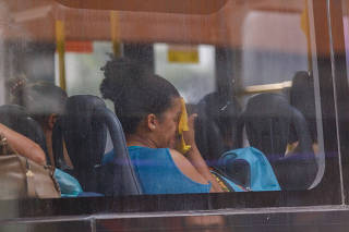 Mulher enxuga o rosto em viagem de ônibus, na cidade de São Paulo