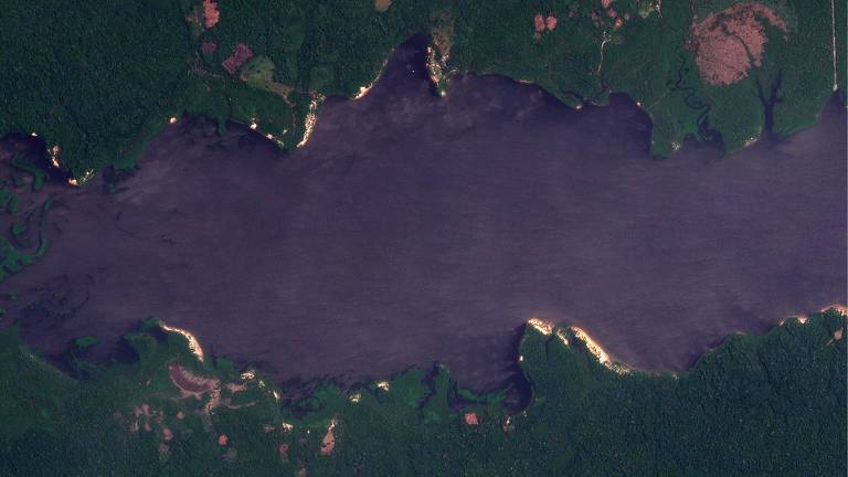 foto aérea mostra leito de rio em tom azul no meio da imagem, cercado por margens verdes de vegetação