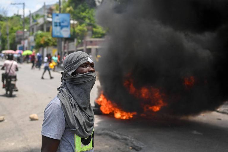 Homem com rosto coberto com camiseta perto de pneus incendiados durante protesto contra insegurança em Carrefour-Feuilles, distrito da capital haitiana, Porto Príncipe