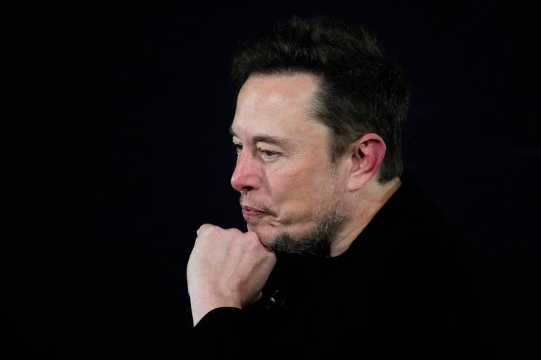 Dono do X, ex-Twitter, Elon Musk faz pausa durante fala em evento com o primeiro ministro britânico Rishi Sunak, em Londres. Musk é um homem branco de cabelos castanhos, barba por fazer e roupa preta.