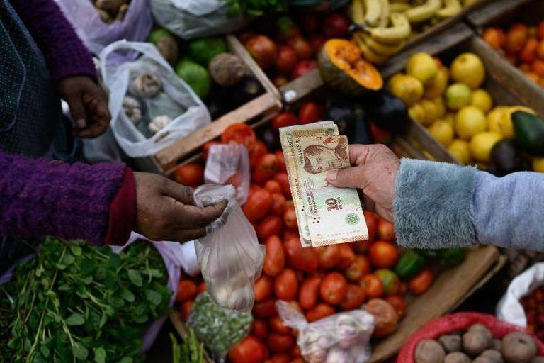 Uma pessoa pagando com pesos argentinos em um mercado de frutas e vegetais