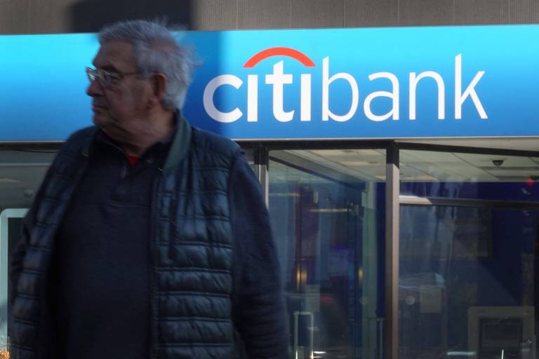 homem grisalho, de óculos, em frente a uma fachada em que se lê Citibank