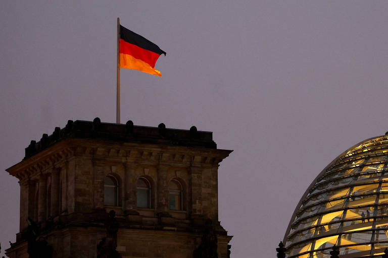 Bandeira da Alemanha hasteada no topo do edifício iluminado do antigo Reichstag, sede do parlamento alemão em Berlim