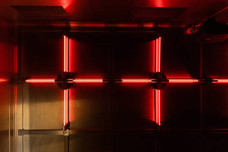 Luminárias vermelhas formam duas cruzes de braços de mesmo tamanho, sobre espelho