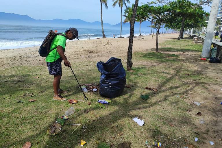 homem com saco de lixo e pá limpa praia