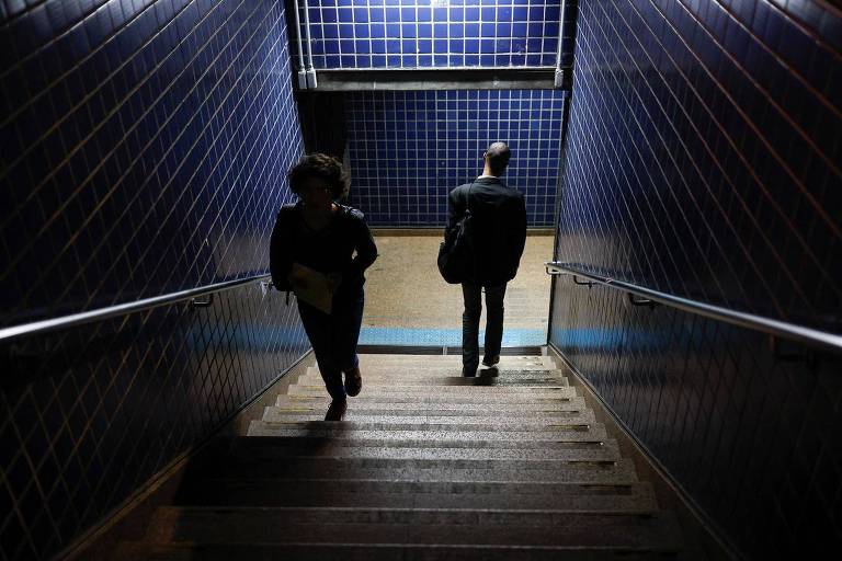 Mulher e homem andando em escada que dá acesso ao metrô em SP